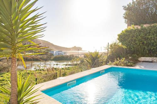 a blue swimming pool with a palm tree in a yard at Bleu Soleil By Ericeira Property in Mafra