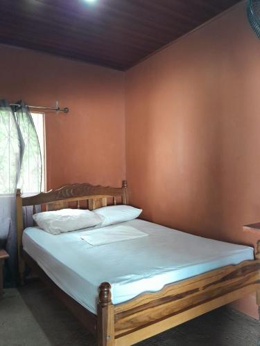 a bedroom with a wooden bed with white sheets at Hostel Los Chocoyos in Ometepe