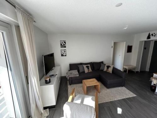 a living room with a black couch and a tv at Charmant appart, avec parking à quelques minutes du départ des télécabines in Crans-Montana
