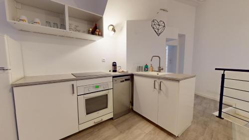 une cuisine avec des armoires blanches, un évier et une cuisinière dans l'établissement Le Nid Caché Mulhouse, à Mulhouse