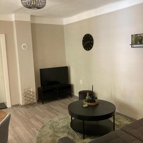 a living room with a table and a clock on the wall at A kis parasztház in Kékesd