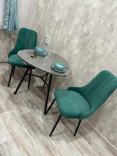 a table with two green chairs and a table with plates at Двухкомнатная уютная квартира in Ekibastuz