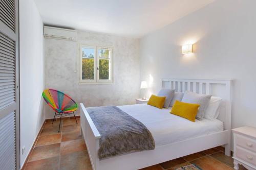 een witte slaapkamer met een bed en een kleurrijke stoel bij Villa Beauregard by Villa Plus in Tourrettes