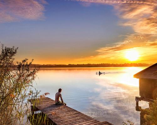 a man sitting on a dock on a lake with a boat at FeWo Frido in Fridolfing
