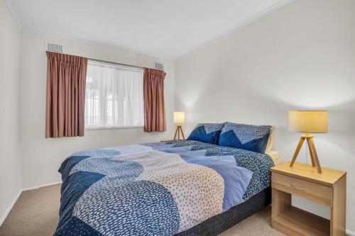 a bedroom with a bed with a blue comforter and a window at 27 Kanangra Street Pambula Beach in Pambula Beach