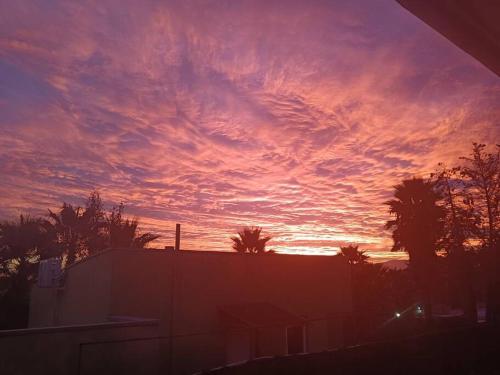 a sunset with a building and palm trees in the sky at Casa en condominio machali, privilegiada in La Viñilla