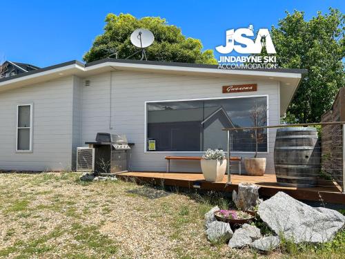a house with a deck with a grill in front of it at Gwenoma in Jindabyne