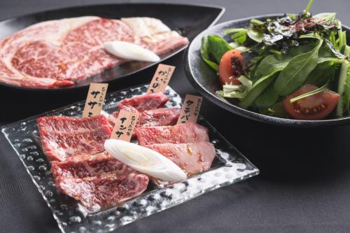 a table topped with plates of meat and a salad at Gotemba Kogen Tokinosumika in Gotemba