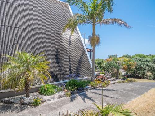 a building with a fence and a palm tree at Ahiparadise - Ahipara Holiday Home in Ahipara