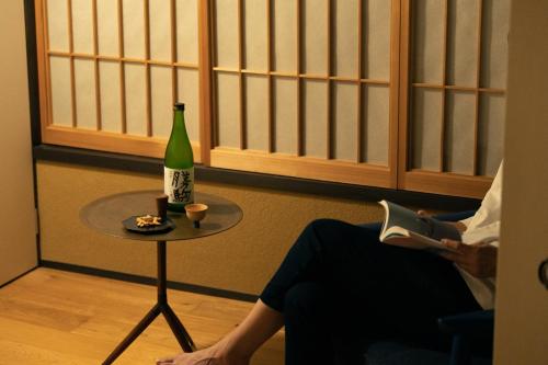 a person sitting in a chair with a bottle and a table at 民家ホテル「金ノ三寸」(かねのさんずん） in Takaoka