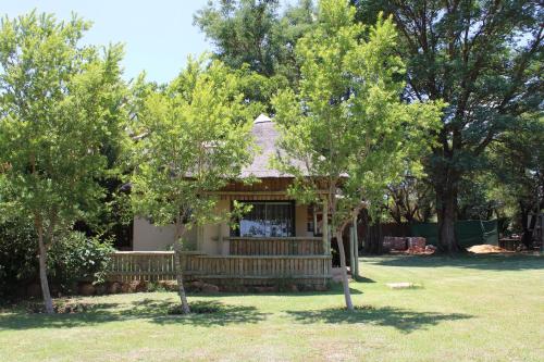 a house with a bench in a yard with trees at Honey Lodge in Klipdrift