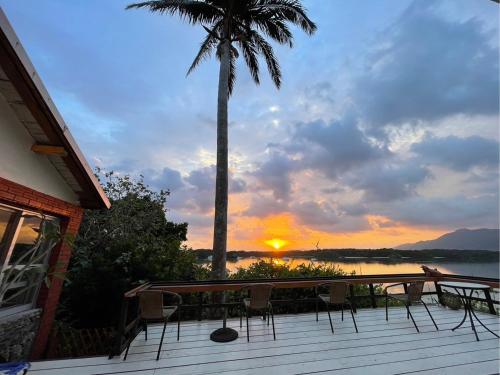 a deck with chairs and a palm tree and a sunset at MAETAKAYA しまんちゅ in Ishigaki Island