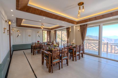 a dining room with tables and chairs and windows at SaffronStays Alpine blue-6 bhk villa with private deck and valley views from each room in Shimla