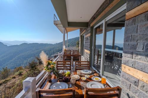 a dining table on the balcony of a mountain house at SaffronStays Alpine blue-6 bhk villa with private deck and valley views from each room in Shimla