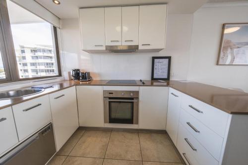 a kitchen with white cabinets and a sink at Duporth - Luxury Riverfront Apartment in Maroochydore