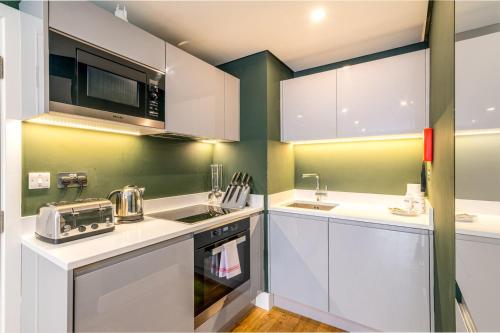 a kitchen with white cabinets and green walls at Trendy Kings Cross Flat in London