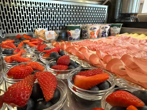 a buffet with bowls of strawberries and blueberries and ham at Hotel Garnì Maffei in Pinzolo