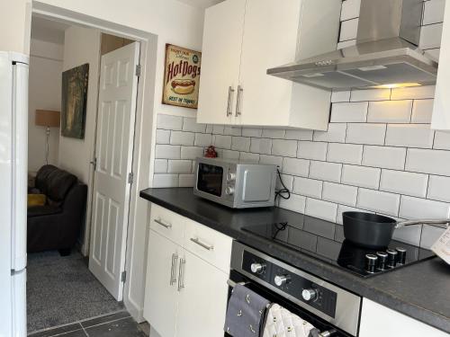 a kitchen with white cabinets and a microwave at Modernised central Wigan townhouse sleeps up to 6 in Wigan
