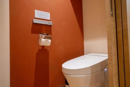 a toilet in a bathroom with an orange wall at ORI Kyoto in Kyoto