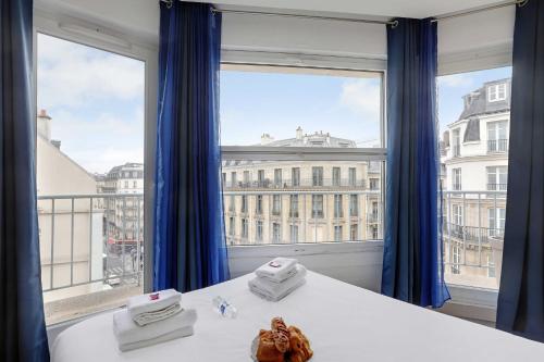 Cette chambre dispose d'une grande fenêtre avec des rideaux bleus. dans l'établissement Résidence Saint-Lazare, à Paris