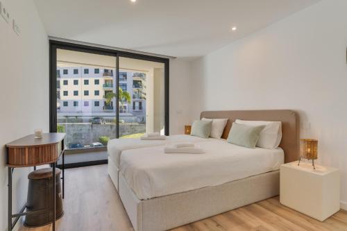 a white bedroom with a large bed and a window at Atlantic Heights Varandas do Atlântico by Holiday Rental Madeira in Câmara de Lobos