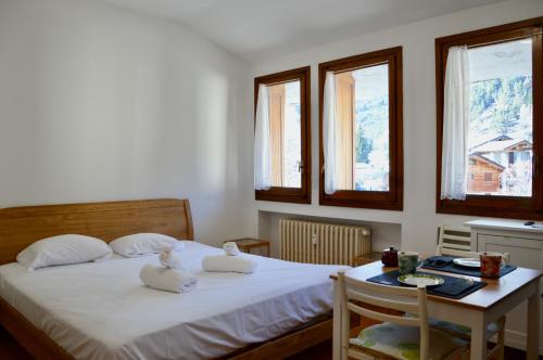 a bedroom with a bed and a table and windows at Hostdomus - Florence Apartments in Cesana Torinese