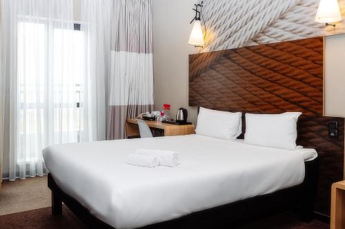 a hotel room with a large white bed and a desk at Ibis Aktobe in Aktobe