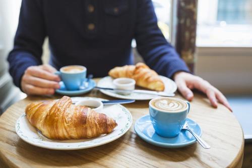een persoon aan een tafel met kopjes koffie en croissants bij Al Cortile in Santa Maria di Licodia