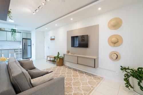 a living room with a couch and a tv on a wall at Apartamentos em Bal Piçarras 150 M DA PRAIA com Sacada Wi Fi, Piscina, Portaria 24h, Playground e vaga de GARAGEM in Piçarras