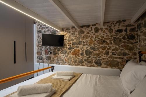 a room with a bed and a tv on a stone wall at Agali Luxury Stone Suite & Loft in Mokhós