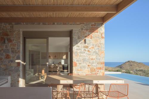 a patio with a table and chairs and a stone wall at VK Villas - Votsalo & Kyma Villas, By ThinkVilla in Léntas
