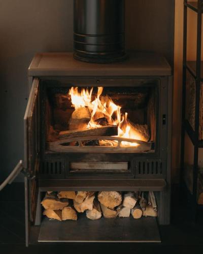 a stove with fire in it with logs in it at Briežu Stacija Off Grid Cabin in Līgatne