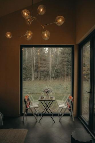 a table and chairs in a room with a large window at Briežu Stacija Off Grid Cabin in Līgatne