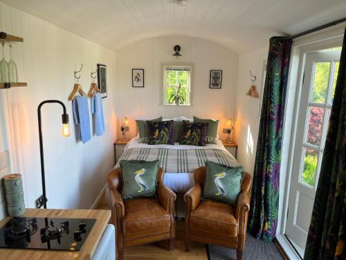 a bedroom with a bed and two leather chairs at Broombush B & B & Yr Nyth Shepherds Hut in Aberhafesp