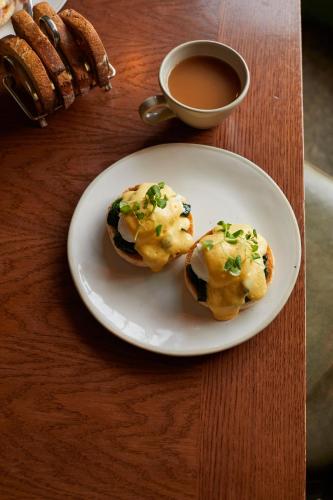 two muffins on a plate next to a cup of coffee at The Royal Forest - A Heartwood Inn in Chingford