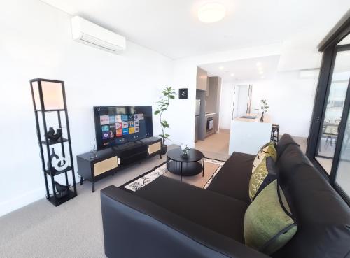 a living room with a black couch and a flat screen tv at Horizon Suite on the TOP in Olympic Park in Sydney