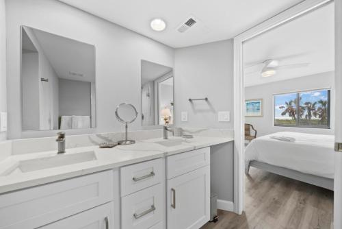 a white bathroom with two sinks and a bed at Sandpiper Beach 101 in Sanibel