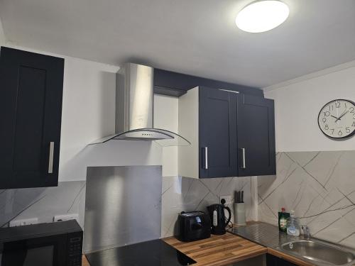 a kitchen with black cabinets and a clock on the wall at Cosy Studio in Heart of Bridgend in Coity