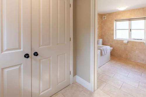The Cow Barn - Norfolk Cottage Agency في Banningham: حمام به باب أبيض وحوض استحمام