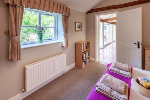 The Cow Barn - Norfolk Cottage Agency في Banningham: غرفة نوم بسرير أرجواني ونافذة