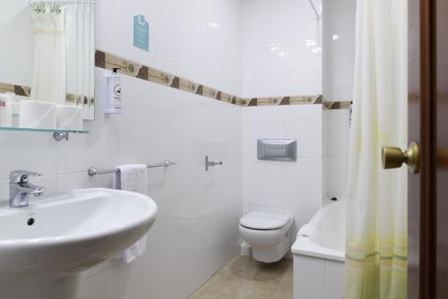 a white bathroom with a sink and a toilet at Hotel Alda Narón in Narón