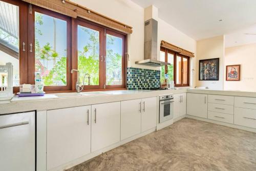 a kitchen with white cabinets and large windows at Art Luxe Homes Chiang Mai in Doi Saket
