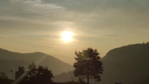 a sun in the sky with trees and mountains at Thuring's Holiday Bungalow in Nuwara Eliya