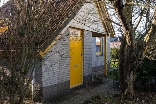 a yellow door on a brick house with a tree at Tulip Beach in De Zandloper