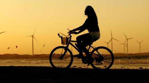 a woman riding a bike on the beach with windmills at Pousada La vida boutique in Icaraí