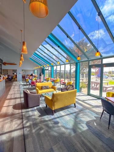 a lobby with yellow chairs and tables and windows at JetPark Hamilton Airport New Zealand in Hamilton