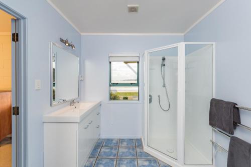 a white bathroom with a shower and a sink at Taupo Bay Beach House in Totara North