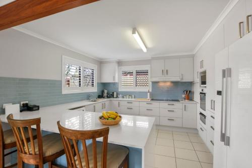 a kitchen with white cabinets and a bowl of fruit on a table at Bren Place, 6, Battery Hill in Caloundra