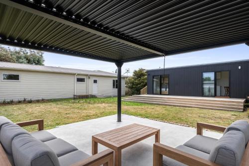 a patio with couches and a table under a pergola at Coastal Family Escape - Waitarere Beach Retreat in Levin