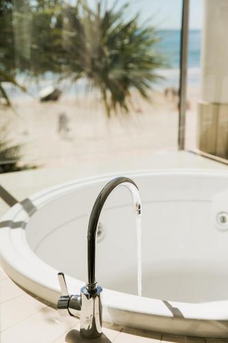 a bath tub with a faucet next to a beach at On The Beach Noosa Resort in Noosa Heads